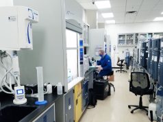 A scientist in a lab coat examines a vial labeled with an experimental cancer drug in a modern laboratory setting.