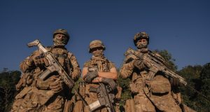 India Suspends Indus Waters Treaty After Pahalgam Attack Indian and Pakistani soldiers stand near a canal along the Indus River, with water flowing between dry banks under a hazy sky.