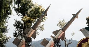 Iran-Israel Direct Fire Reshapes Middle East Smoke rises from a building after an airstrike in a Middle Eastern city, with debris scattered on the street.
