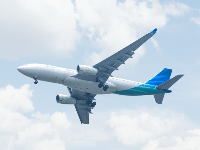 A Boeing 737 Max 9 aircraft parked on a tarmac with maintenance crew inspecting the fuselage near the door plug area.