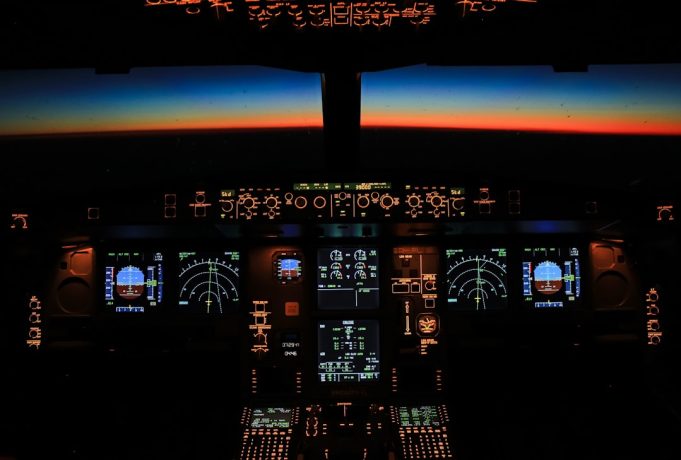 Airbus Cites Solar Radiation in Emergency Software Update for A320 Fleet Technician uploads new code to an A320 cockpit computer inside a dim hangar while the jet’s tail fin glows under bright hangar lights.