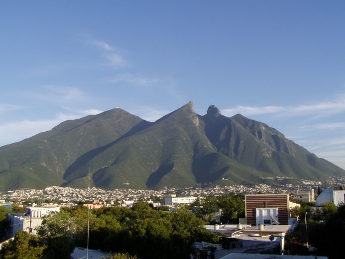 Van Crash in Mexico Kills Twelve and Injures Four Others Nearby A burned van lies at the bottom of a ravine in Nuevo León, Mexico, with smoke rising from a small wildfire in the surrounding forest.
