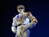 A humanoid robot running on a Beijing race course, crossing a finish line with spectators watching.