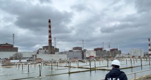 IAEA Deploys Teams to All Ukraine Nuclear Plants IAEA Director General Rafael Grossi stands with Ukrainian officials at a nuclear plant, raising the agency's flag beside Ukraine's flag.