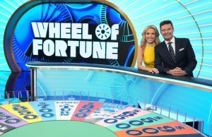 Ryan Seacrest Takes Wheel of Fortune Host Role Ryan Seacrest and Vanna White standing at the Wheel of Fortune puzzle board, smiling at the camera.
