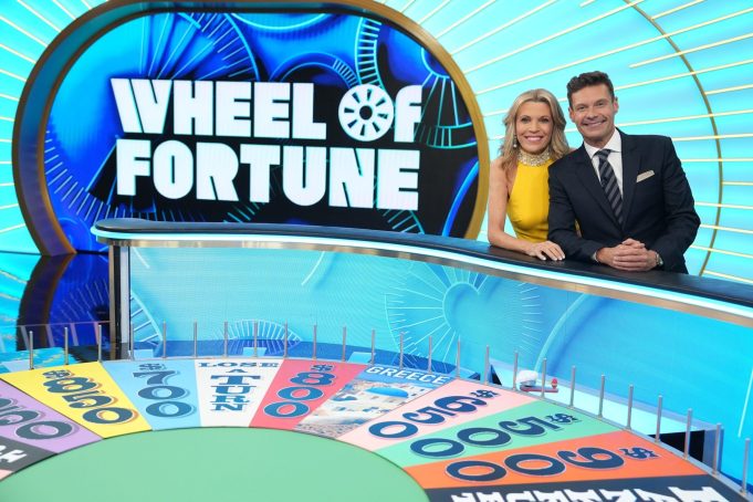Ryan Seacrest Vanna White Wheel Fortune Ryan Seacrest and Vanna White standing at the Wheel of Fortune puzzle board, smiling at the camera.