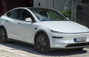 A Tesla vehicle with Full Self-Driving software drives through Austin streets with a safety monitor in the front passenger seat.