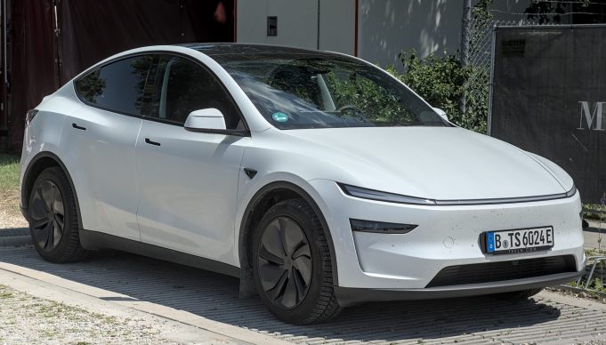 A Tesla vehicle with Full Self-Driving software drives through Austin streets with a safety monitor in the front passenger seat.
