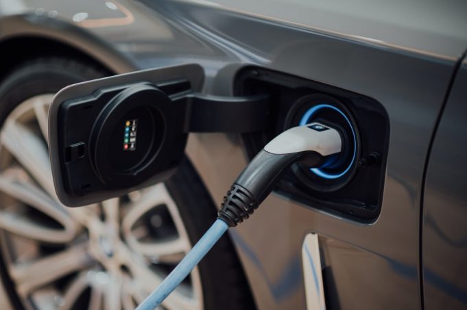 China's Tiny Wuling Hongguang Mini EV Surpasses 1.1 Million Global Sales A small Wuling Hongguang Mini EV parked on a busy Chinese city street, surrounded by pedestrians and larger vehicles.