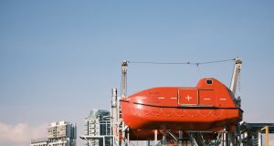 RESQSHIP Saves 59 from Coffin Dinghy, 3 Children Die Overcrowded gray inflatable dinghy adrift on open sea as orange rescue vessel approaches