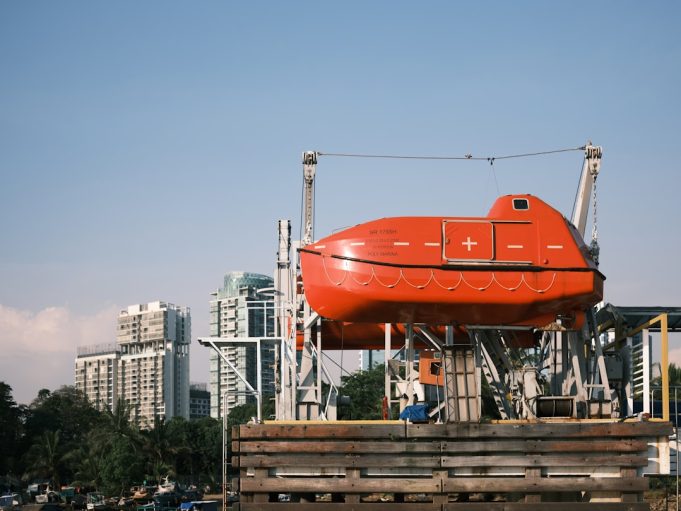 Overcrowded gray inflatable dinghy adrift on open sea as orange rescue vessel approaches