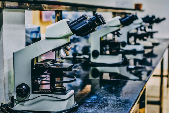 A scientist in a lab coat examines a vial labeled Yeztugo lenacapavir under bright laboratory lights.